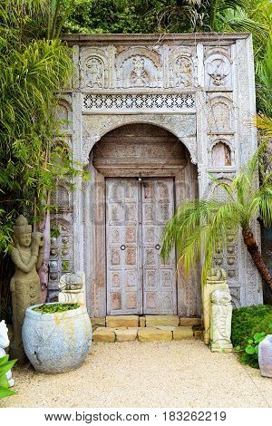 Rustic style wooden door made from bamboo wood surrounded by lush green tropical plants taken in a residential garden