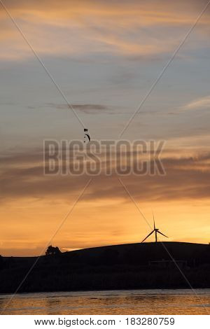 Wind turbine with power parachute flying over in the delta at sunset