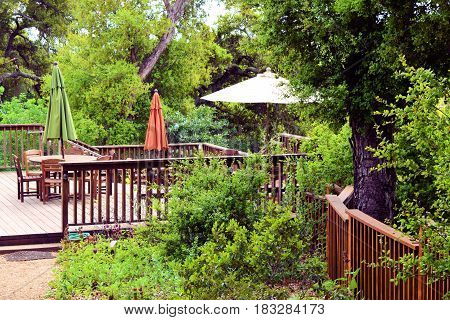 contemporary rustic style wooden deck with outdoor furniture surrounded by a lush green forest taken in a residential garden