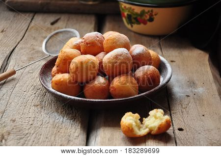 Small balls of freshly baked homemade cottage cheese doughnuts in a plate on a wooden background. Rustic style.