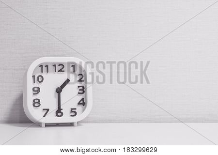 Closeup white clock for decorate show half past one o'clock or 1:30 p.m. on white wood desk and cream wallpaper textured background in black and white tone with copy space