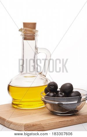 Glass cruet with Extra virgin olive oil, canned black olives in bowl stand on a wooden cutting board on a white background.