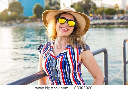 summer holidays, vacation, travel and people concept - smiling laughing young woman wearing sunglasses and hat on beach over sea background.