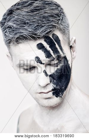 Young man with black hand print on his white face. Close up Portrait.  Professional Fashion Makeup. fantasy art  makeup