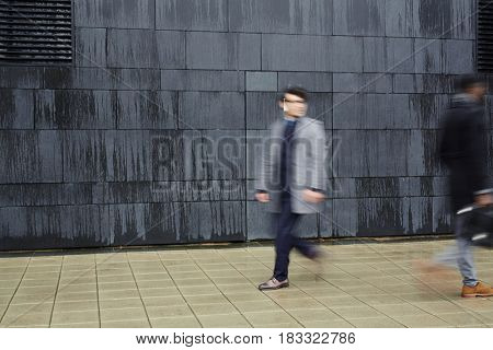 Hurrying men walking down trottoire along black wall of modern building