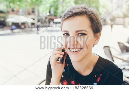 Girl with short pixie haircut is having a phone conversation. People and technology concept. Making phone calls talking to  friends discussing plans for summer.
