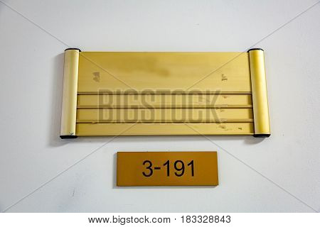 Yellow nameplate with black figures 3-191 hanging on a light wall
