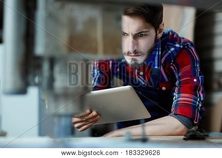 Serious mechanic with touchpad observing work of milling machine