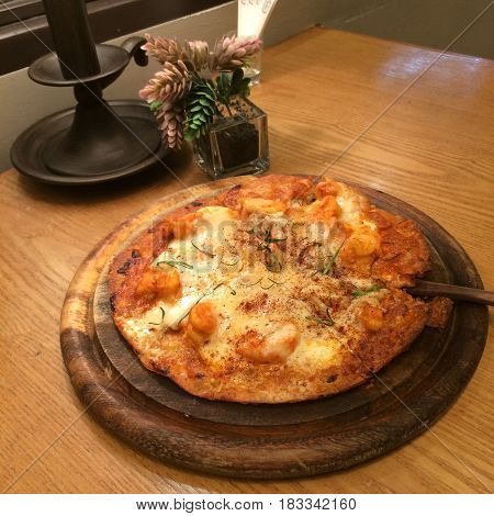 Pizza prawn Tomyum top with cheeses and herbal seafood pizza on the wood tray in restaurant with blur wooden table and decoration Thai pizza