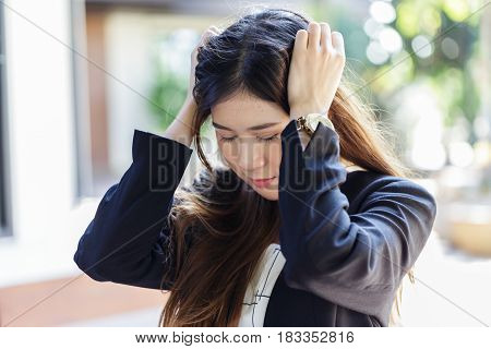 Pretty Asian young business woman with headache, holding both of her hands to her head. Trying hard to focusing on her work, feeling stressful and exhausting.