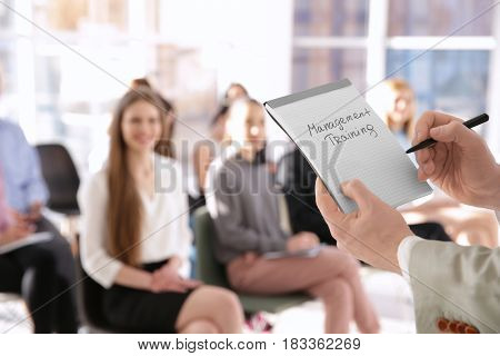 Business trainer holding notebook with text MANAGEMENT TRAINING at presentation