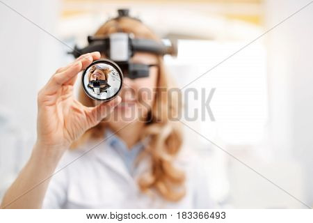 Important equipment. Nice clever professional doctor using indirect ophthalmoscope while conducting a procedure for diagnosing her patient