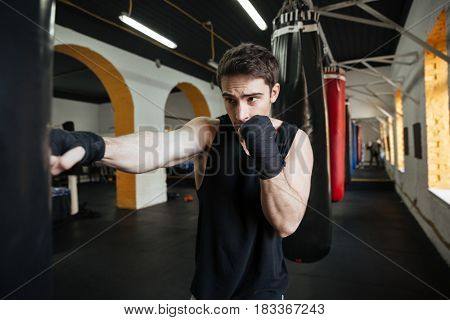 Concentrated boxer doing training in gym with punchbag