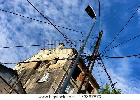 A lot of electric wires to a pole in the city on the background of blue sky and houses