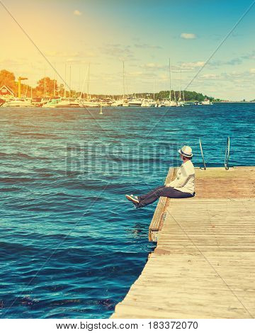 Girl in hat sitting on pier and lookingat the river