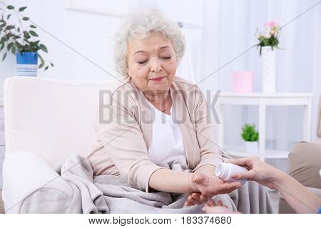 Elderly woman taking pills in light room