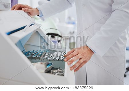 Give ear-funnel. Young doctor standing near medical tools choosing the necessary one while going to work with it