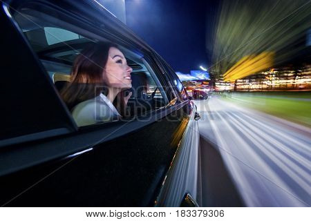 Moving towards the nightlife in the city, woman on the backseat of a car