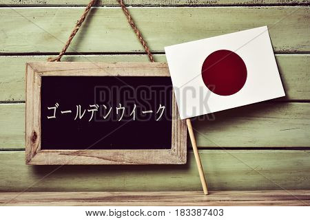 a blackboard with the text golden week written in japanese and a flag of japan, against a pale green rustic wooden background