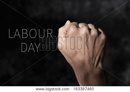 closeup of the raised fist of a young man against a gradient dark gray background and the text labour day