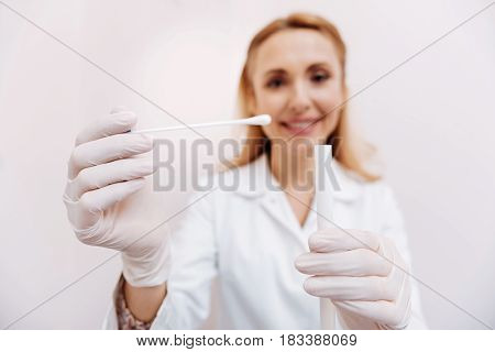  Positive delighted pediatrician keeping smile on her face standing on the background while looking straight at camera