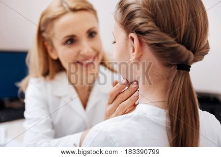  Positive delighted doctor touching neck of her patient while looking straight into eyes, keeping smile on her face
