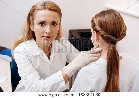  Serious pediatrician pressing her lips doing examination of her patient while looking straight at camera