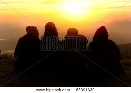 Silhouette of friends sitting down and looking at the sunrise together