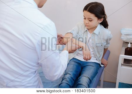 Visit to a rheumatologist. Nice cute serious girl holding her arm up and being examined by a rheumatologist while visiting a hospital