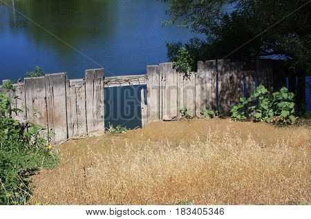 Hole in the fence leading to beautiful blue lake with tree reflections