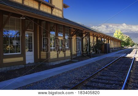 Train station along side train track with blue sky and low clouds in the distance