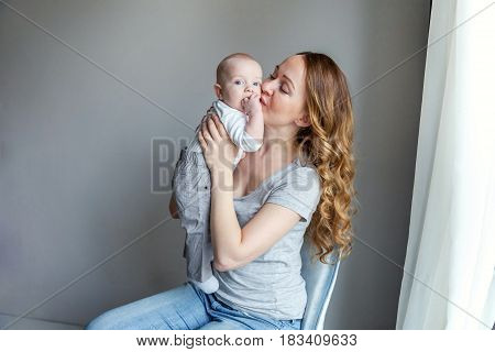 Young mother holding her newborn child. Woman and new born boy relax in a white bedroom with blue chair. Mother breast feeding baby. Family at home. Young mother kissing her newborn son