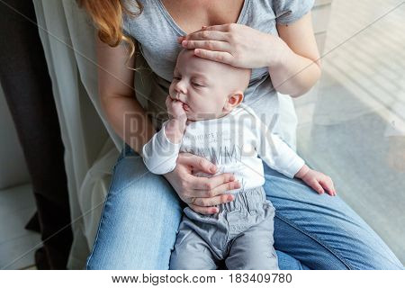Mother holding her newborn child. Woman and new born boy relax near the windiow. Mother breast feeding baby. Family at home. Young mother playing whith her newborn son