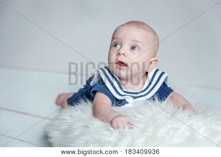 Infant child baby boy In a sailor's suit lies on his stomach on a white pillow against a white wall background