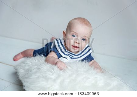 Infant child baby boy In a sailor's suit lies on his stomach on a white pillow against a white wall background