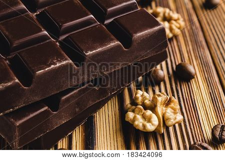Three pieces of bitter dark chocolate bar walnut core and coffee bean on wooden background close-up view.