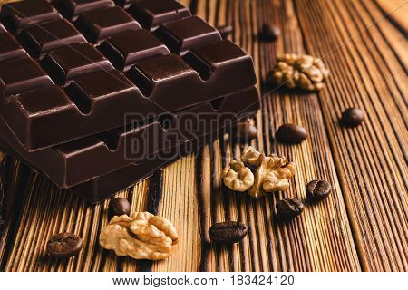 Three pieces of bitter dark chocolate bar walnut core and coffee bean on wooden background close-up view.