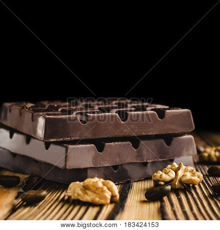 Three pieces of bitter dark chocolate bar walnut core and coffee bean on wooden background close-up view.