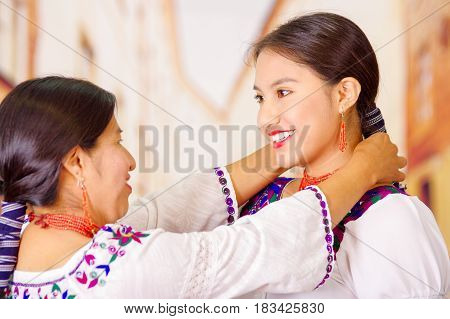 Beautiful portrait of mother with daughter, both wearing traditional andean clothes and matching necklaces, posing embracing happily.