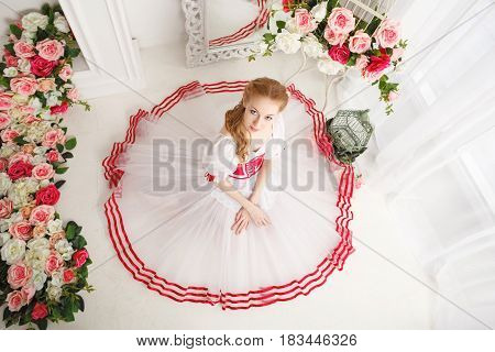 A sweet ballerina in a scenic costume and bouquets of spring flowers. Retro dress. She sits on the floor. High angle shooting