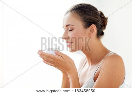 beauty, cosmetics, skin care and people concept - close up of beautiful happy woman holding and smelling cream jar