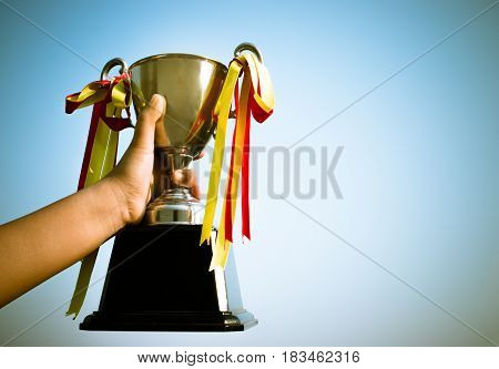 winner and champion concept Hand holding championship trophy against blue sky