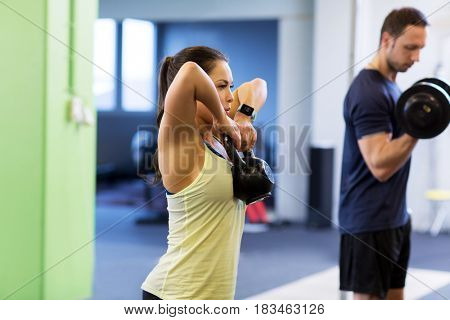 sport, fitness, lifestyle and people concept - woman with kettlebell and man with dumbbell exercising in gym