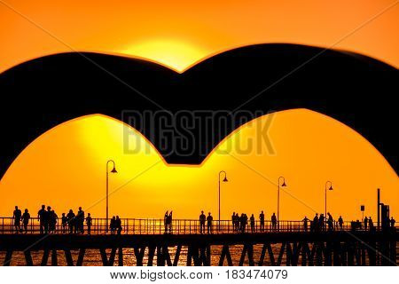 Glenelg beach jetty with people viwed through the heart at sunset