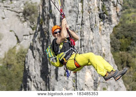 Young male climber hanging on rope and smiling at camera on background of rock