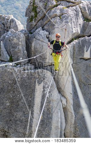 Male climber in special outfit walking rope bridge on big height