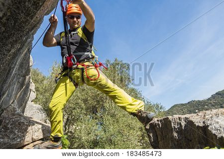 Young male alpinist hanging on rock and smiling at camera