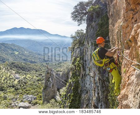 Male climber in special outfit climbing cliff with mountaineering equipment