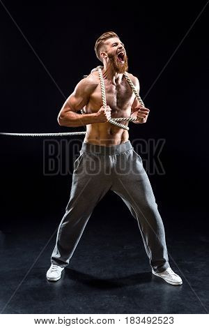 Handsome Bearded Sportsman Yelling And Pulling Rope Isolated On Black
