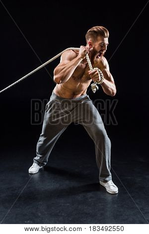 Handsome Bearded Sportsman Yelling And Pulling Rope Isolated On Black